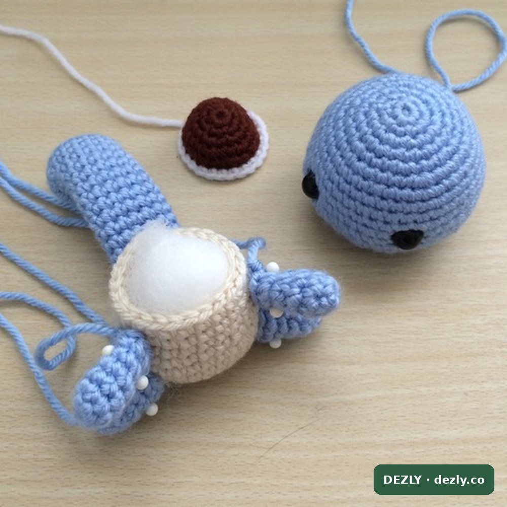 Las piezas de Squirtle en proceso de montaje: el cuerpo crema relleno con la cola y un brazo prendidos con alfileres, con la cabeza y el caparazón al lado.
