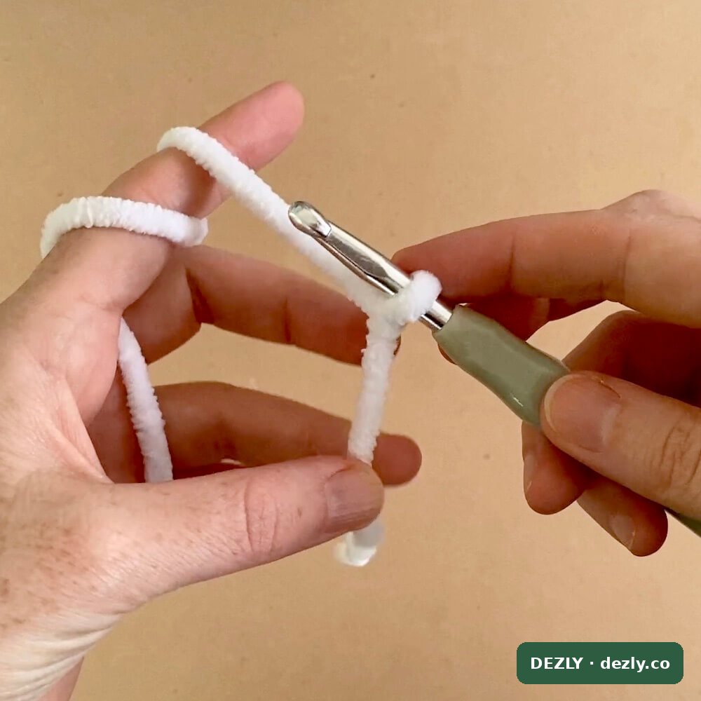 Nudo corredizo en el ganchillo, listo para empezar la cadeneta en hilo chenille blanco.